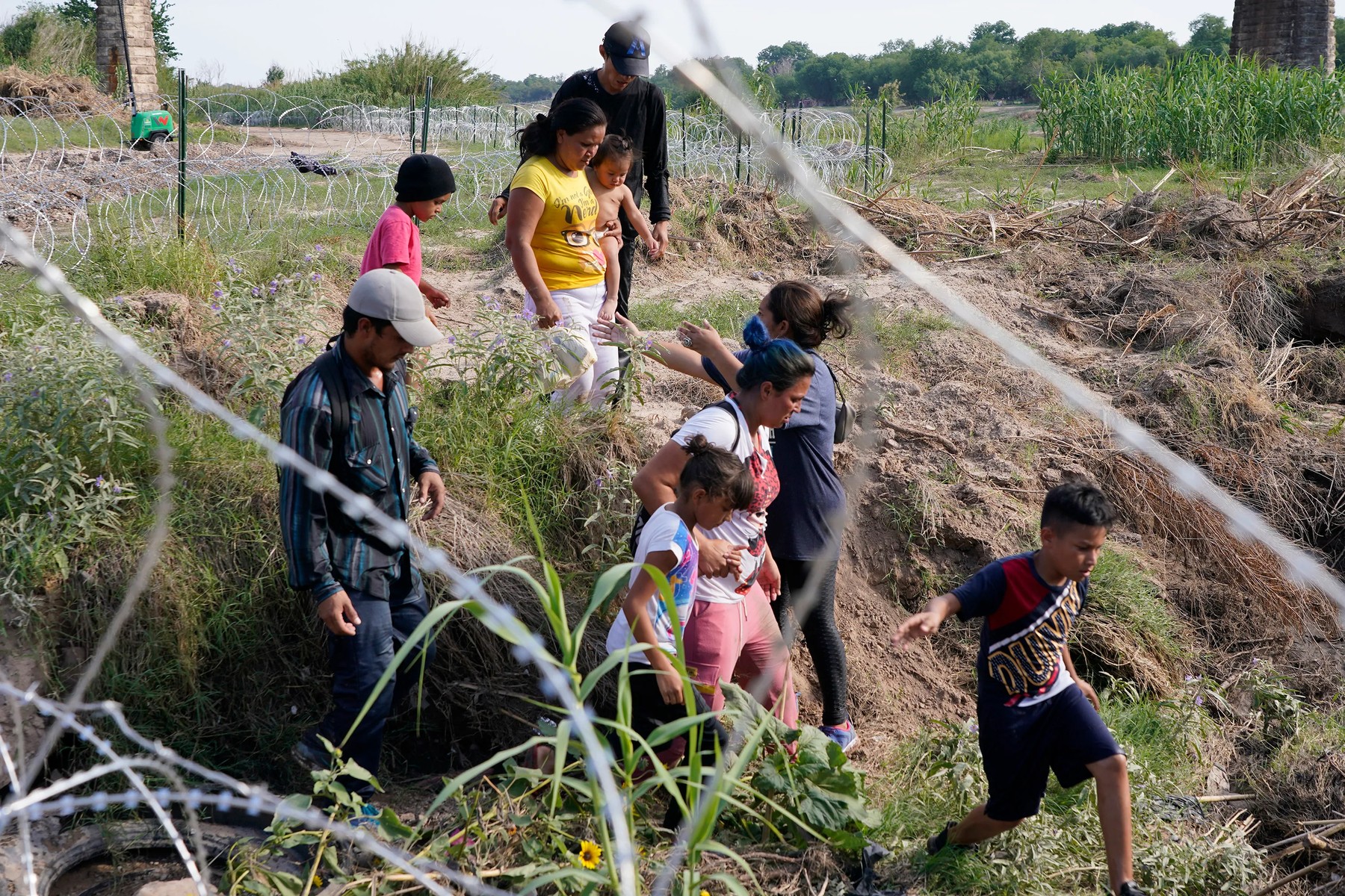 Migrants, most with children, follow a path along the concertina wire where ultimately they will placed under guard by Border Patrol after having crossed the Rio Grande on May 27, 2022 in Eagle Pass, Texas.