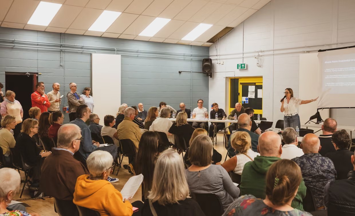 … until local residents, like those at this public meeting in a boxing club, changed his mind